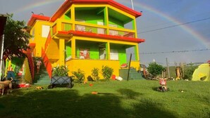 Una casa colorata con un balcone, immersa in un prato verde e un arcobaleno nel cielo.