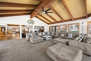 A spacious living room with a high ceiling, a large sofa set, and a dining area. - Grand Lakefront Escape - Lakefront Cabin | Hot Tub, Pool Table (Big Bear Lake)