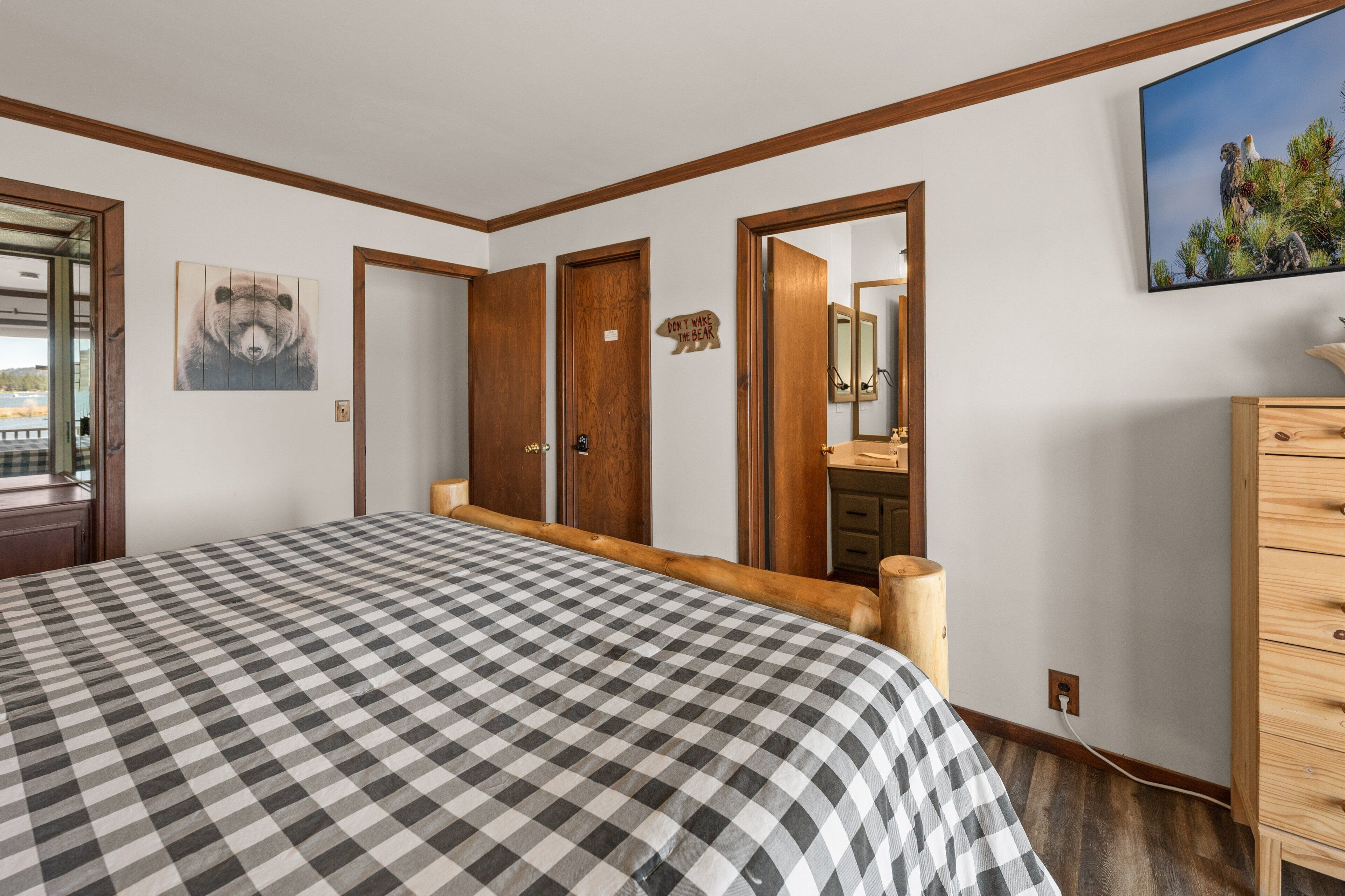 Une chambre à coucher avec une couvre-lit à carreaux, des portes en bois, une commode, un miroir et un tableau accroché au mur.
