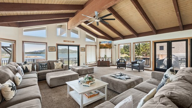 A spacious living area with a large sectional sofa, ottomans, a coffee table, and a view of the lake. - Grand Lakefront Escape - Lakefront Cabin | Hot Tub, Pool Table (Big Bear Lake)