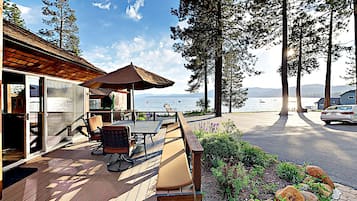 Relax on the deck with a table and chairs, overlooking a tranquil body of water surrounded by tall trees.