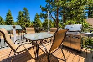 An outdoor patio with a glass table, wicker chairs, and a built-in grill.