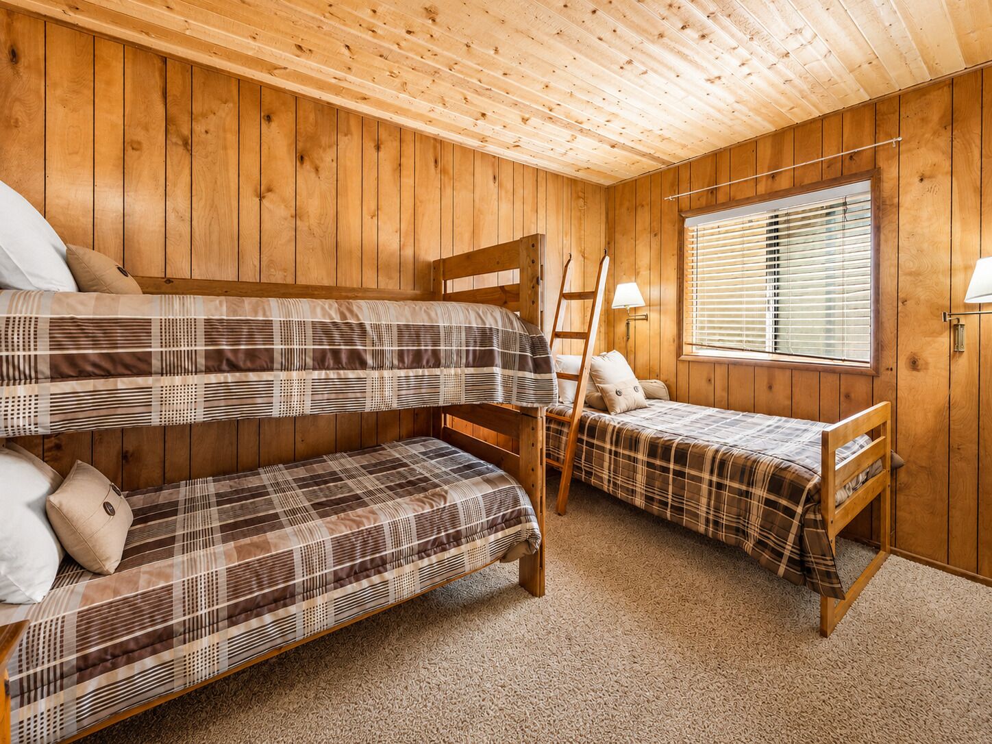 A room with two bunk beds, a window with blinds, a wooden ladder, and a lamp.