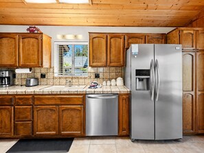 Una cocina con armarios de madera, electrodomésticos de acero inoxidable, dispensador de agua y una ventana con persianas.