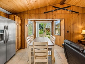 A wooden interior with a dining table, chairs, a sofa, and a refrigerator.