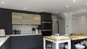 A modern kitchen with dark cabinetry, a wooden backsplash, stainless steel appliances, and a wooden countertop.