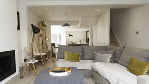 A modern living room with a grey sofa, a wooden ladder, and a remote control on a tray.