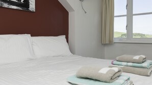 Ein ordentlich bezogenes Bett mit weißen Leinen und Blick auf eine grüne Landschaft durch ein Fenster.