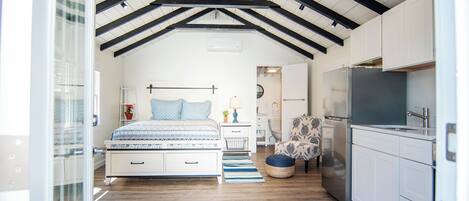 Un dormitorio con una cama grande, mesitas de noche, una silla y una kitchenette con refrigerador.