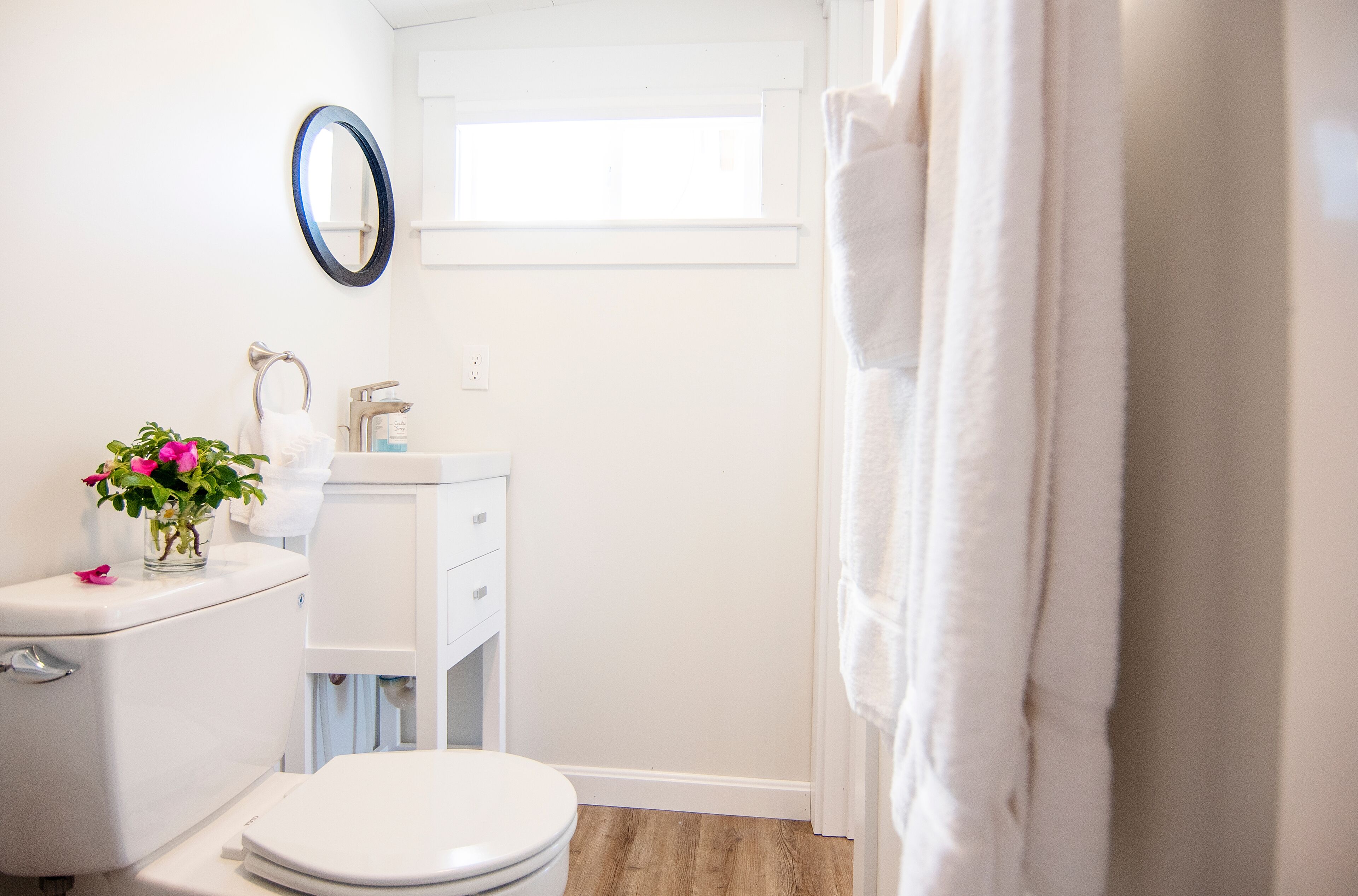 A bathroom with a toilet, sink, and mirror. There is a window above the sink and a towel hanging on the wall.