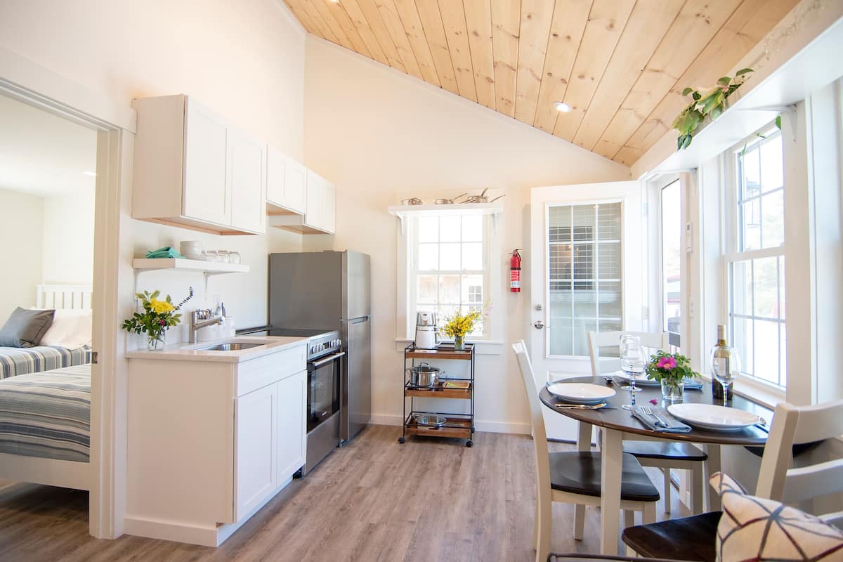 A modern kitchen with white cabinetry, a wooden ceiling, and a dining area with a table set for two.