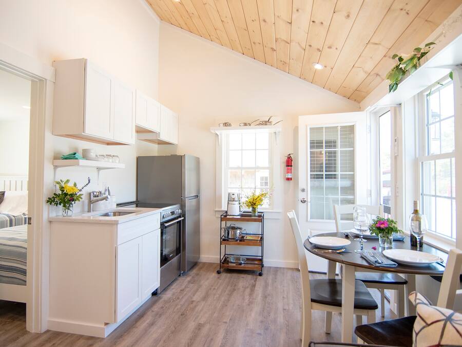 Een moderne keuken met witte kastjes, een houten plafond en een eethoek met een tafel gedekt voor twee personen.
