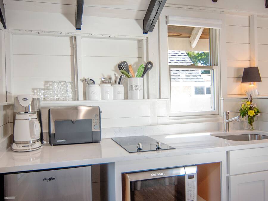 A modern kitchen with a built-in dishwasher, a coffee maker, and a toaster. There is a window with a view of a house and a lamp on the countertop.