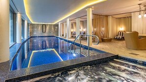 A hotel lobby with a large indoor pool, seating area, and a staircase leading to the upper floors.