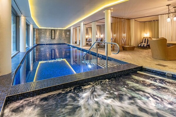 A hotel lobby with a large indoor pool, seating area, and a staircase leading to the upper floors.