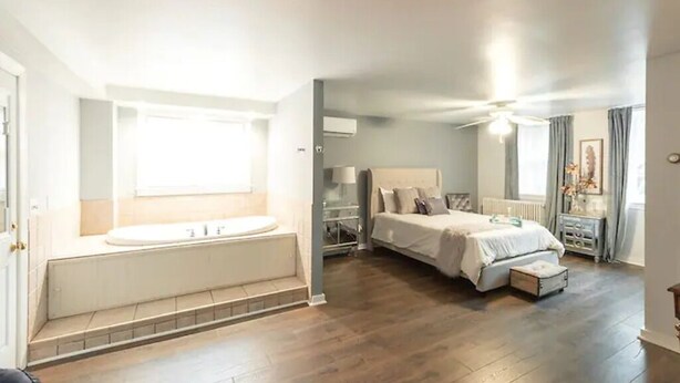 A bedroom with a large bed, a built-in bathtub, and a ceiling fan.