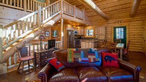 A log cabin interior with a wooden staircase, a living room with leather furniture, a kitchen with modern appliances, and a dining area. - Armstrong Lxury Vacation Home at Windcliff (Estes Park)