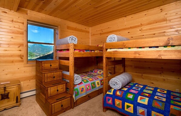 Una cabaña con tres camas literas, un tocador de madera y una ventana que ofrece vistas a la montaña.