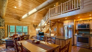 A log cabin interior with a dining area, kitchen, and a staircase leading to an upper level. - Armstrong Lxury Vacation Home at Windcliff (Estes Park)