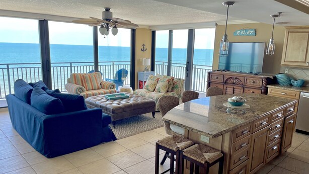 A spacious living area with a large window overlooking the ocean, a cozy seating arrangement, and a kitchen with wooden cabinets.