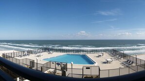 A pool area with a view of the ocean, surrounded by a fence and lounge chairs.