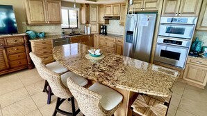 A kitchen with a large island, built-in appliances, and wicker bar stools.