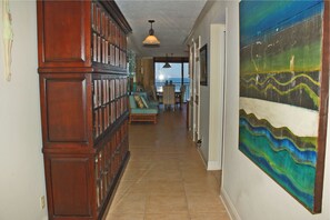 Cozy hallway with a bookcase, cushioned bench, and chair, featuring a large abstract painting and a tiled floor.