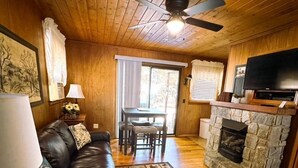Interior acogedor de una cabaña con sofá de cuero, chimenea de piedra, televisor y ventilador de techo.
