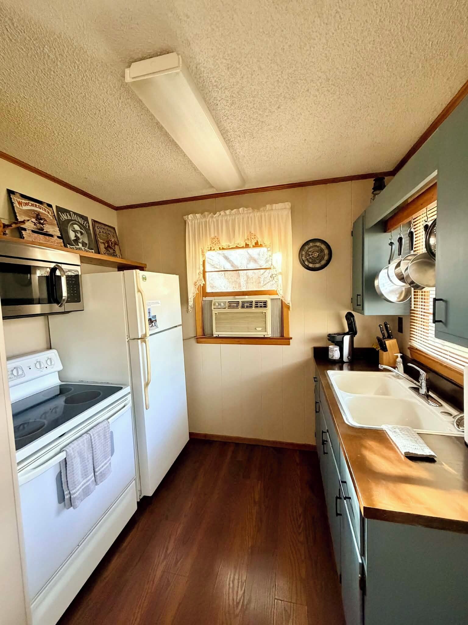 Cocina compacta con estufa, horno, microondas, refrigerador, lavamanos y ventana con cortinas.