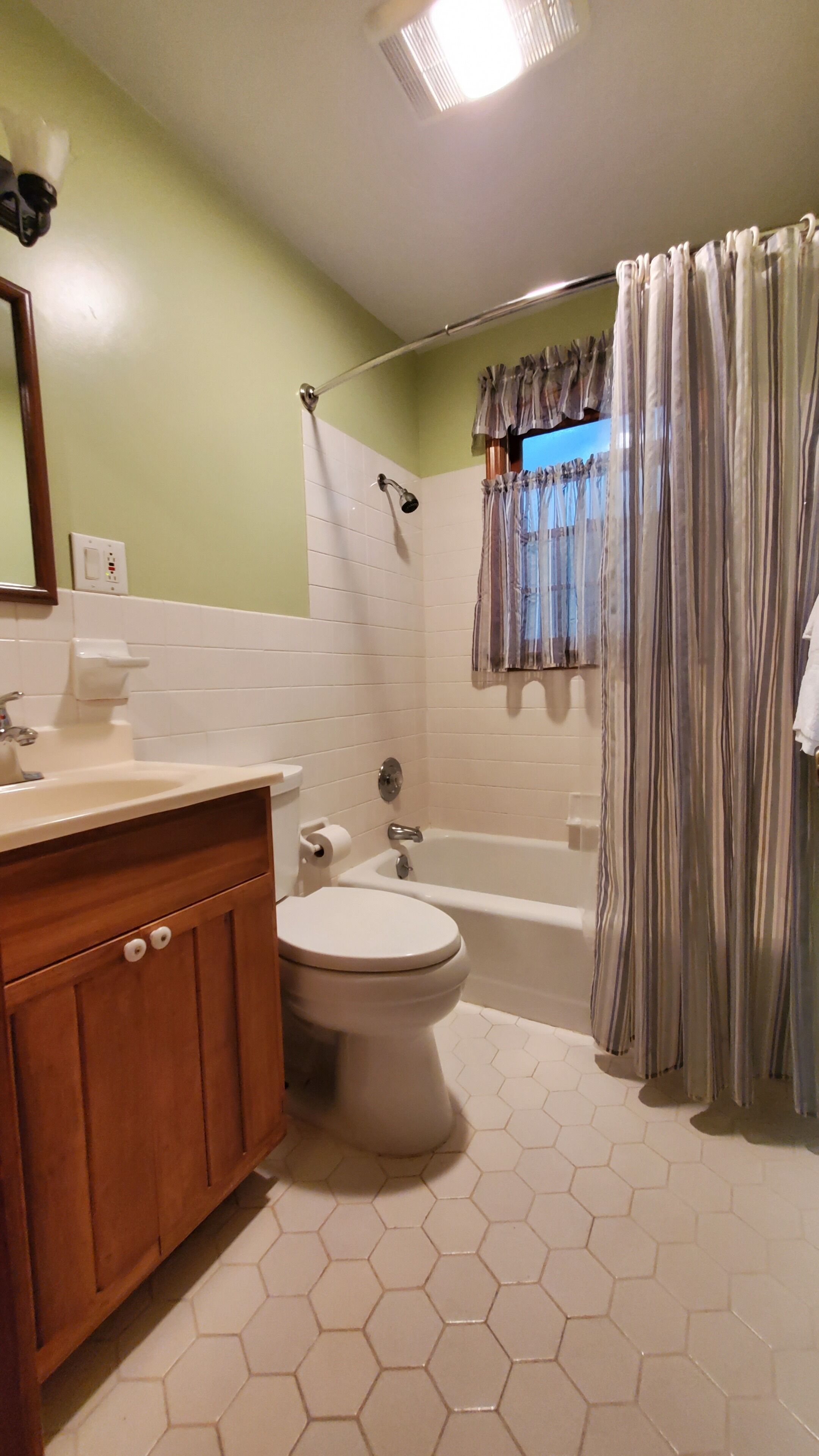 A bathroom with a toilet, sink, shower, and a window with curtains.