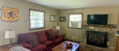 A living room with a sofa, armchair, coffee table, fireplace, television, and a wall-mounted emblem.