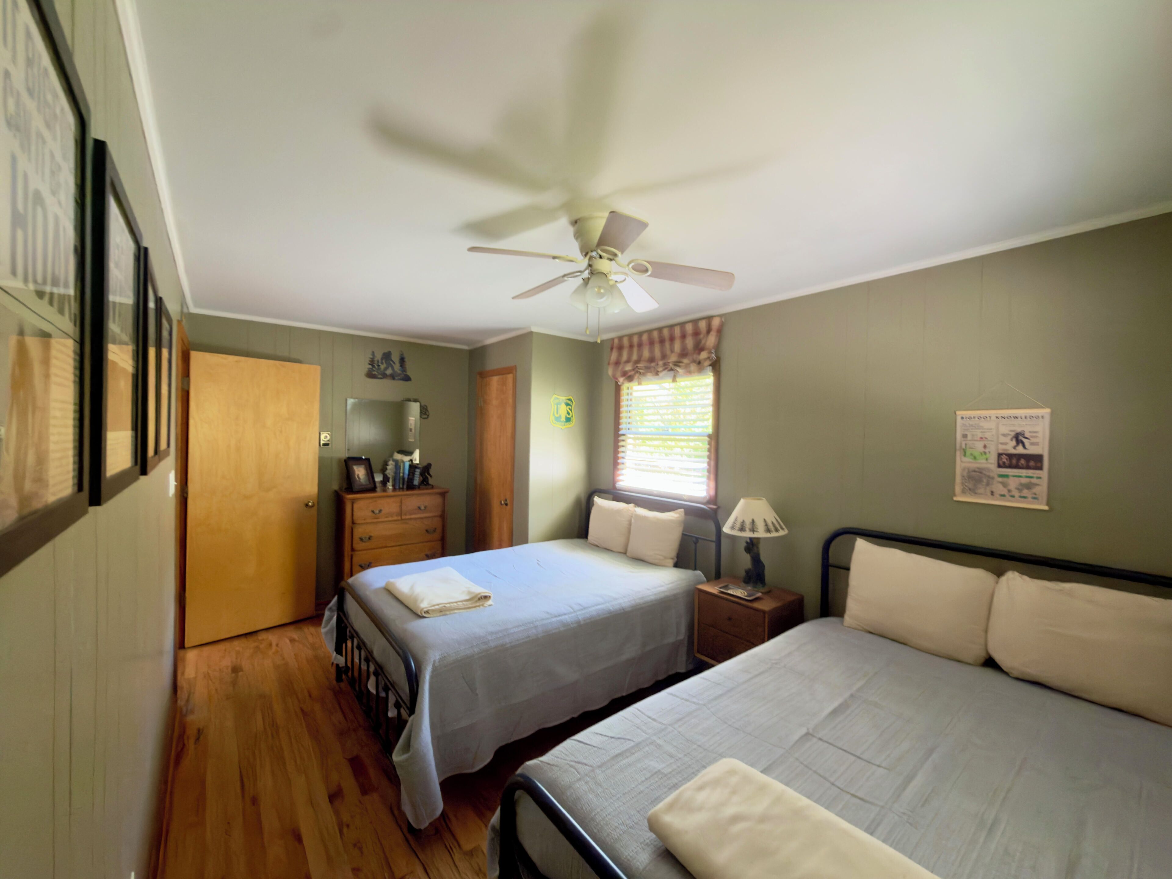A bedroom with two beds, a ceiling fan, a dresser, a window with blinds, and a wall poster.