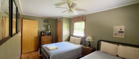 A bedroom with two beds, a ceiling fan, a dresser, a window with blinds, and a wall poster.