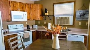 Una cocina con gabinetes de madera, microondas, estufa y una mesa de comedor con sillas.