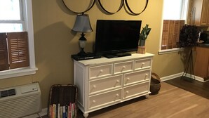 Una sala de estar con un televisor de pantalla plana sobre un tocador blanco, una lámpara y tres espejos colgados en la pared.