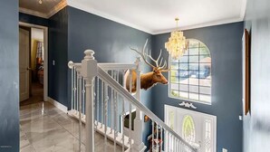 A grand staircase with a mounted deer head, a chandelier, and a stained glass window. - Gorgeous Colonial House on the Water w/ Pool & Jacuzzi
 (Jacksonville)
