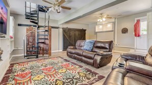A spacious living room with a brown leather sofa, a patterned rug, a spiral staircase, and a ceiling fan. - Gorgeous Colonial House on the Water w/ Pool & Jacuzzi
 (Jacksonville)