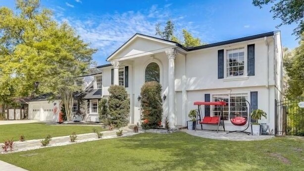 A two-story house with a white exterior, a covered porch with red seating, and a well-maintained lawn. - Gorgeous Colonial House on the Water w/ Pool & Jacuzzi
 (Jacksonville)