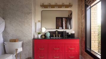 A bathroom with a red vanity, a mirror, a toilet, and a window with a view.