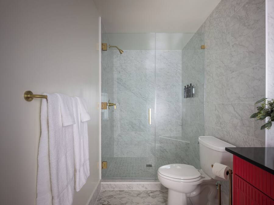 Een badkamer met een douchecabine van glas, een toilet en een wastafel met een rode kast.