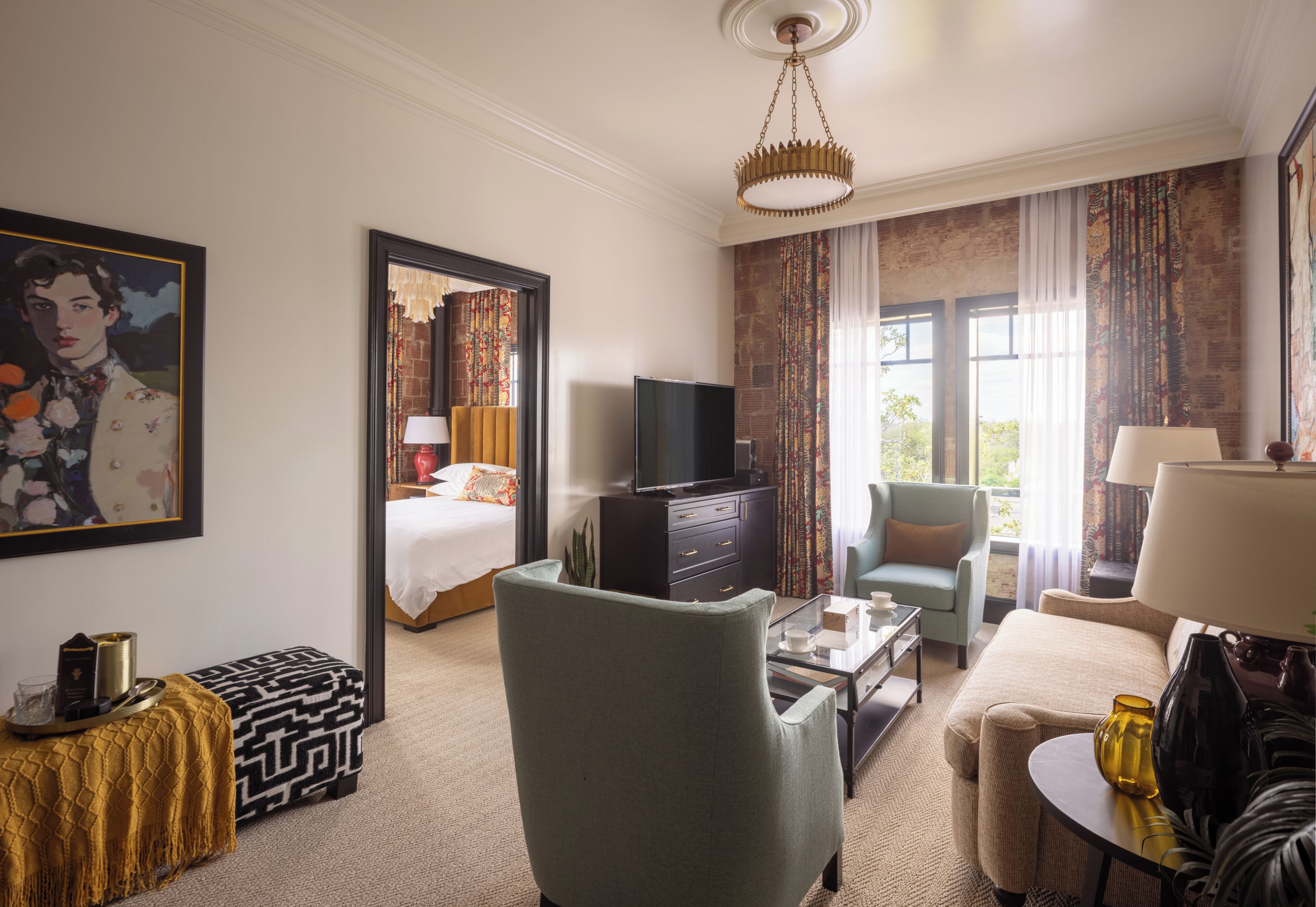 Una habitación de hotel con cama, televisión, sofá, sillón, mesa de centro y lámpara.