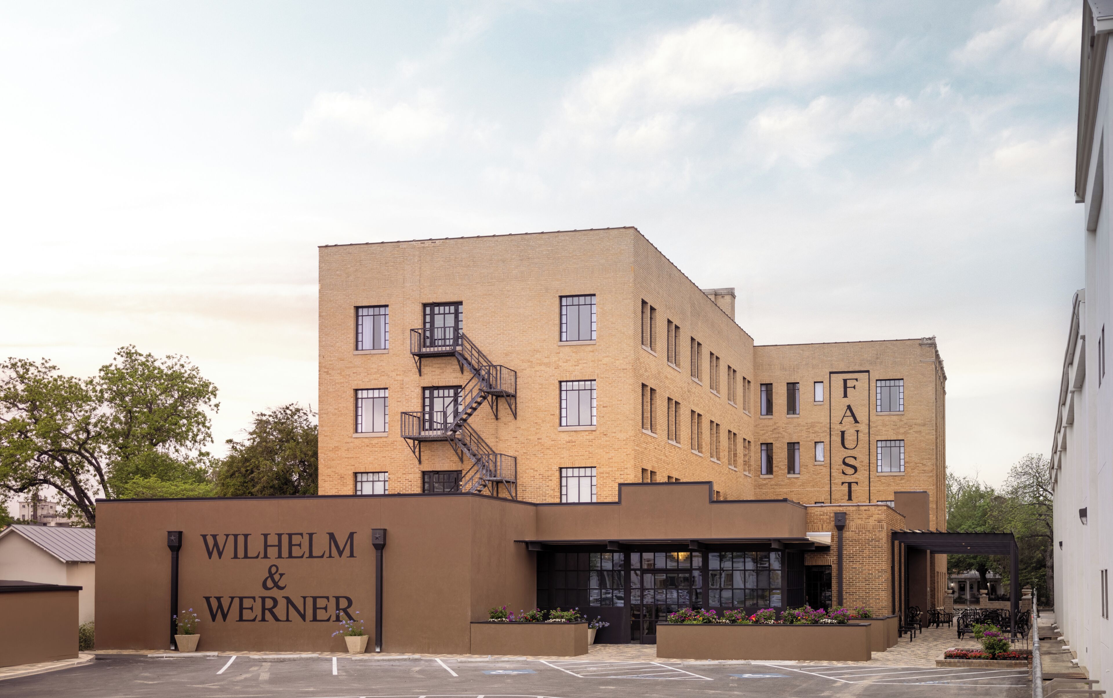 Un edificio de varios pisos con una escalera de incendios, un letrero que dice 'Wilhelm & Werner' y una zona de entrada cubierta con macetas.
