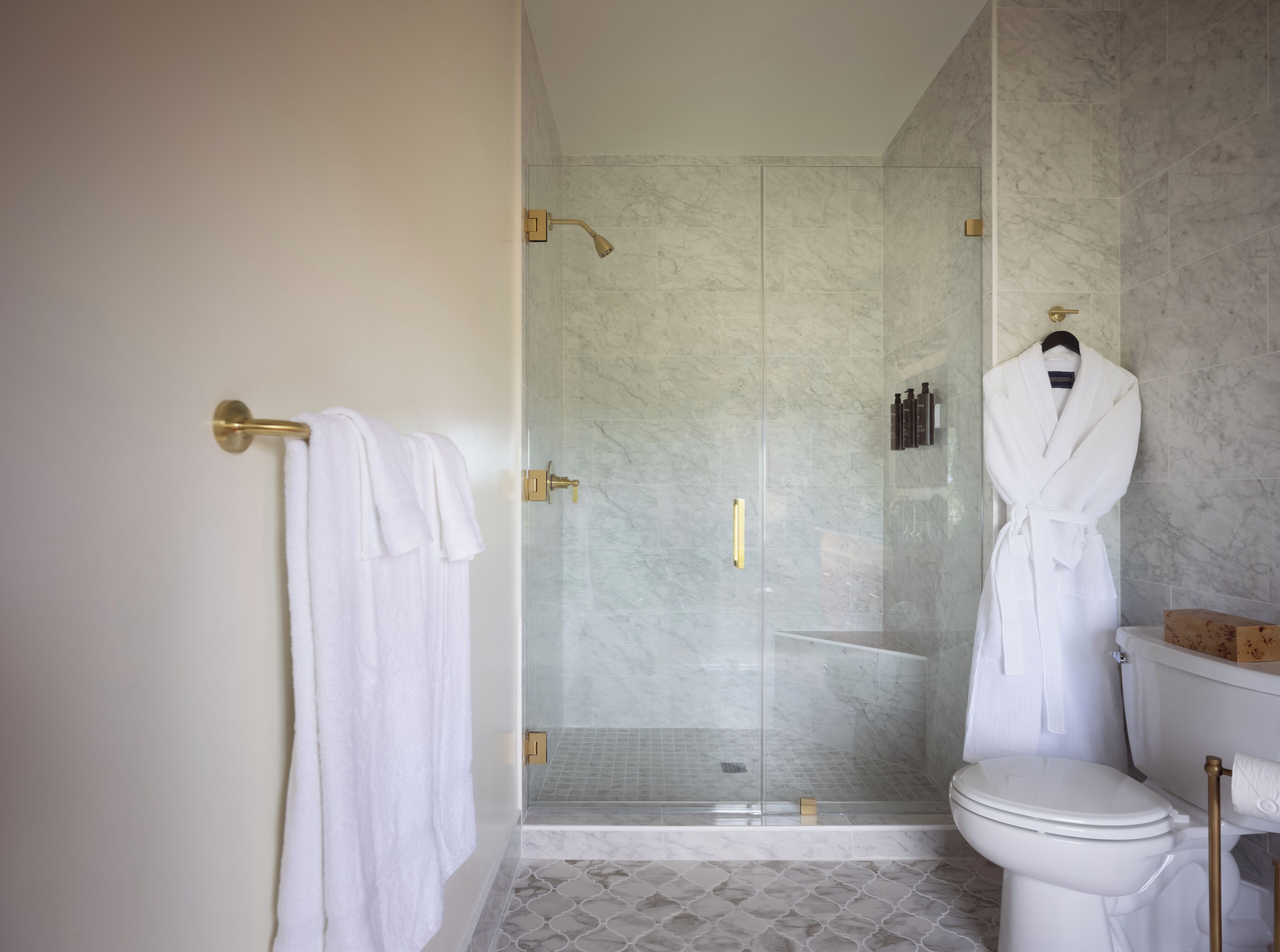 A bathroom with a glass-enclosed shower, a toilet, and a robe hanging on a hook.