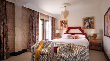 Una habitación de hotel con una cama grande, dos sillones estampados, un candelabro y un cuadro en la pared.