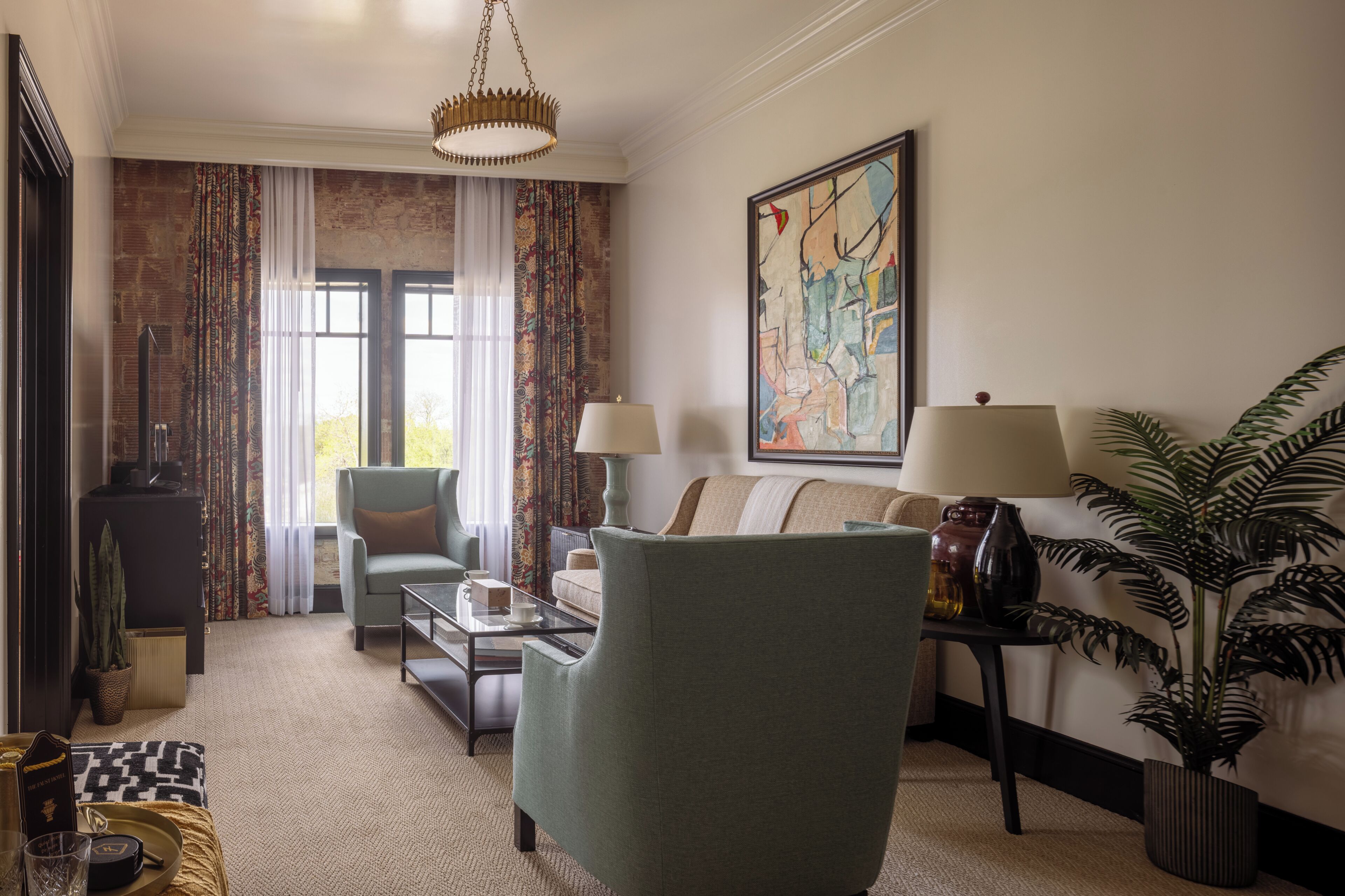 A living room with a sofa, armchairs, a coffee table, lamps, a painting, and a potted plant.
