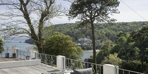 A balcony with a view of a coastal area, trees, and a distant building.