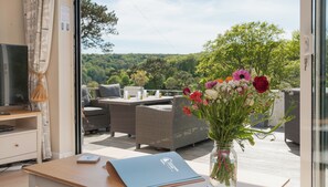 A modern room with a laptop on a table, a vase of flowers, and a view of a lush garden through large windows.