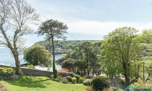 A coastal landscape with a stone wall, lush greenery, and a view of the sea.
