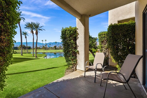 A patio area with a view of a golf course, a pool, and mountains in the background.