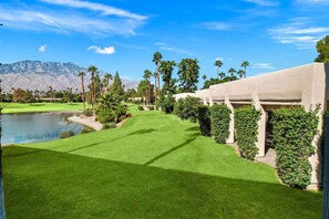 A well-maintained golf course with a pond, palm trees, and a mountain backdrop.